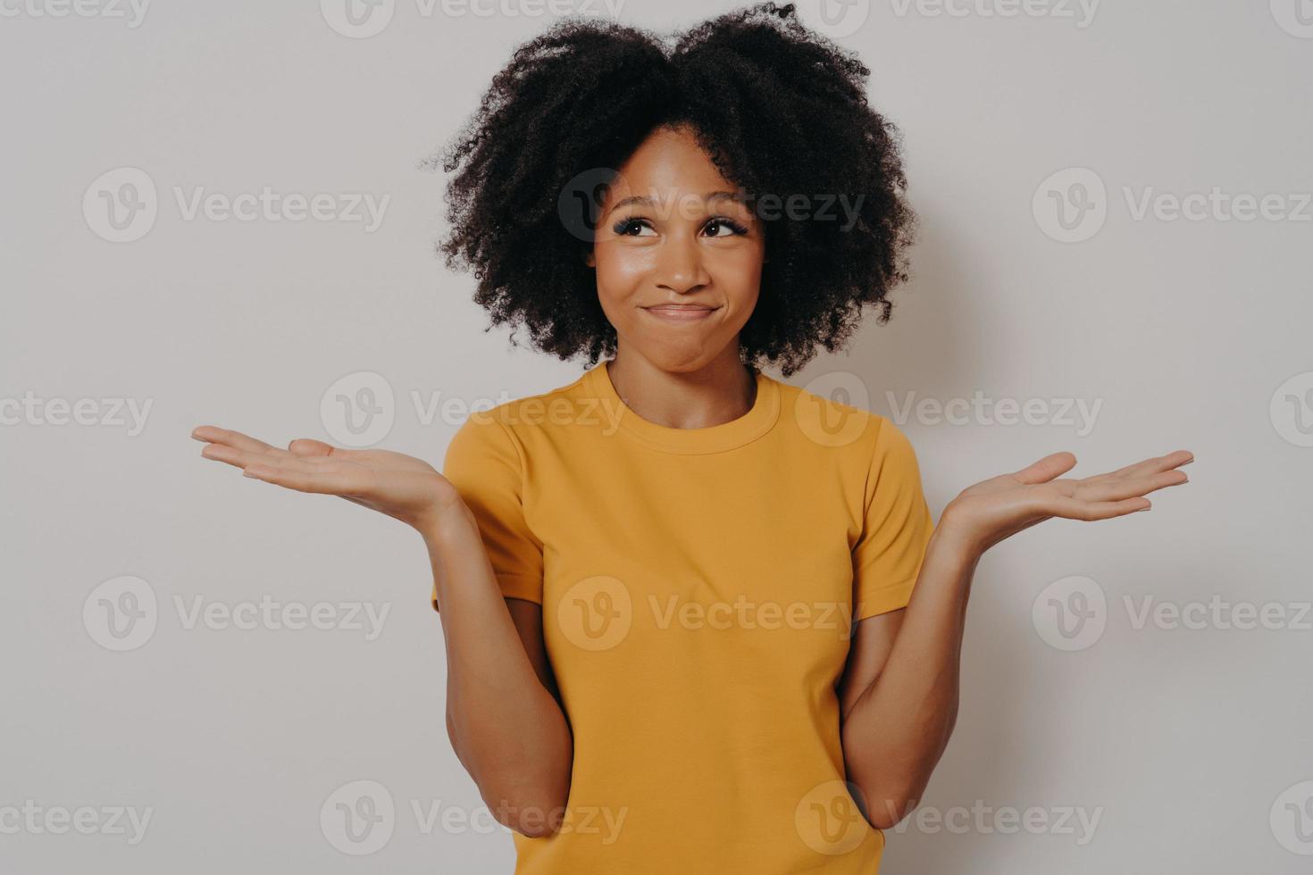 junge afrikanische frau, die mit ahnungslosem und lustigem verwirrtem ausdruck mit erhobenen armen und händen steht foto