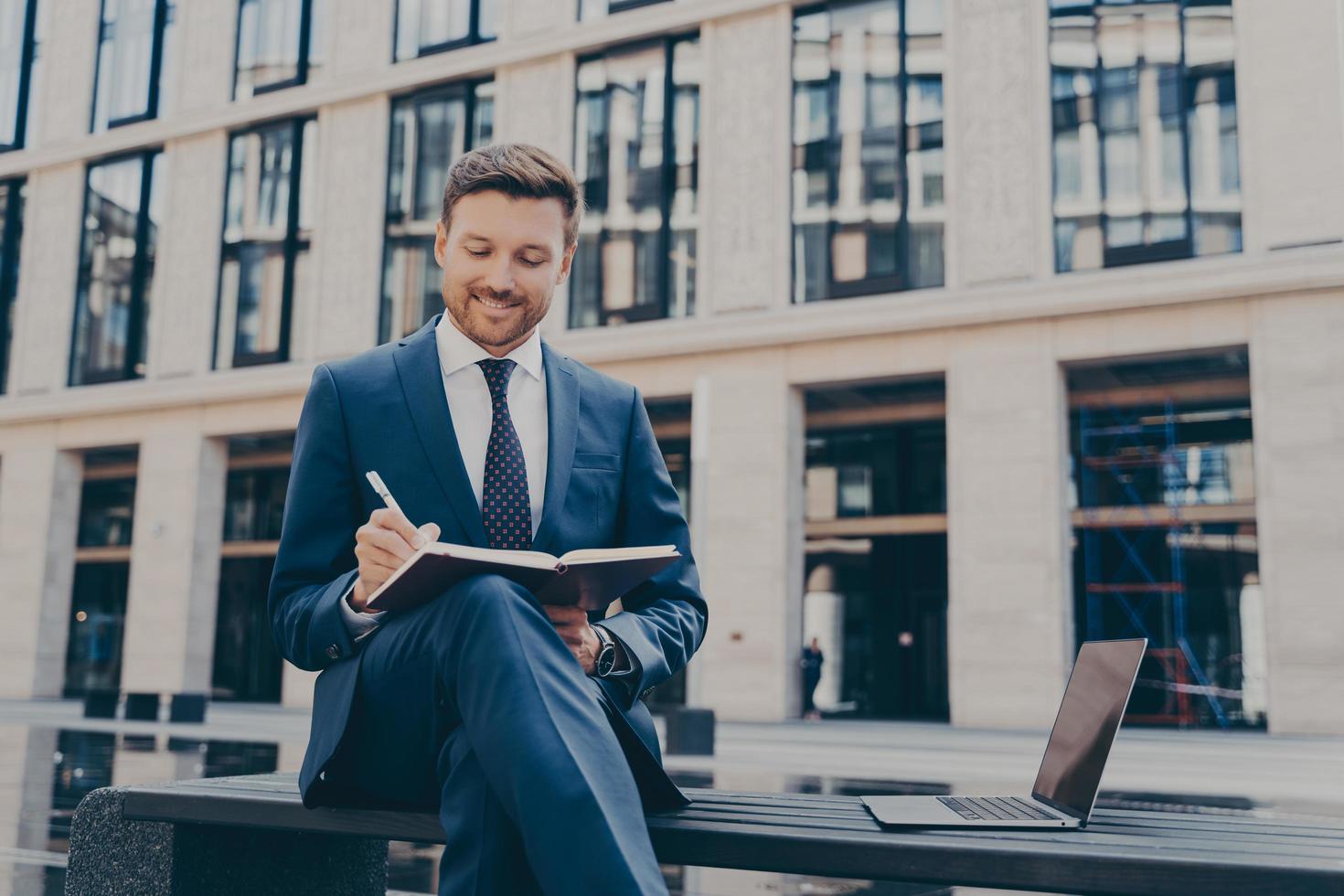 Professioneller Büroangestellter schreibt Ideen in ein Notizbuch, während er online im Freien arbeitet foto