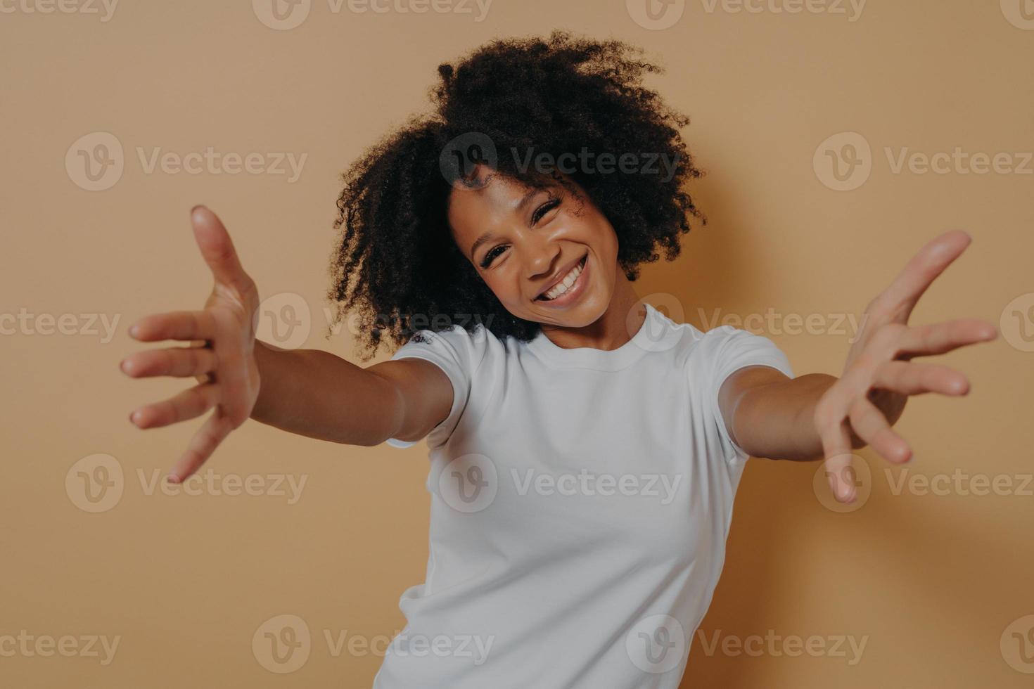 Fröhliche, freundliche afroamerikanische Frau in weißem Hemd, die Umarmungen anbietet und den Kunden willkommen heißt foto