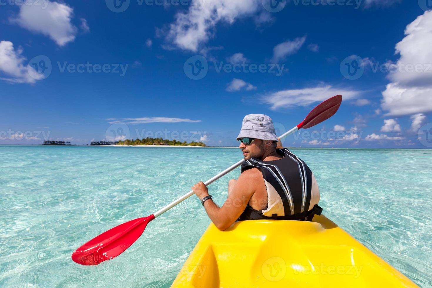 junger kaukasischer Mann, der im Meer auf den Malediven Kajak fährt foto