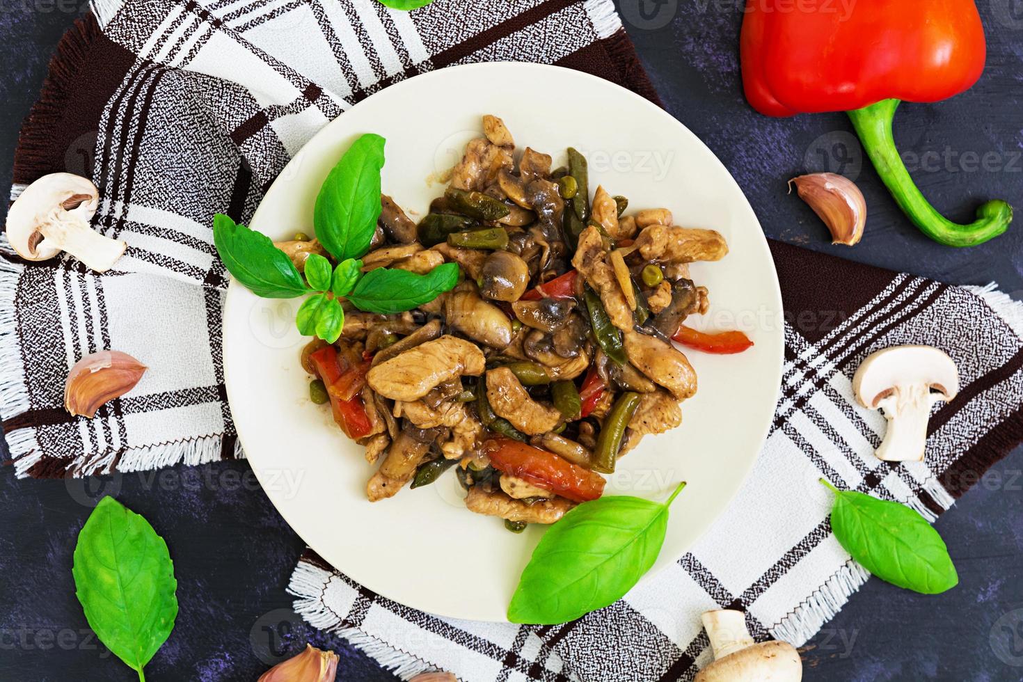 Brathähnchen mit Paprika und Erbsen auf dunklem Hintergrund rühren. Ansicht von oben foto