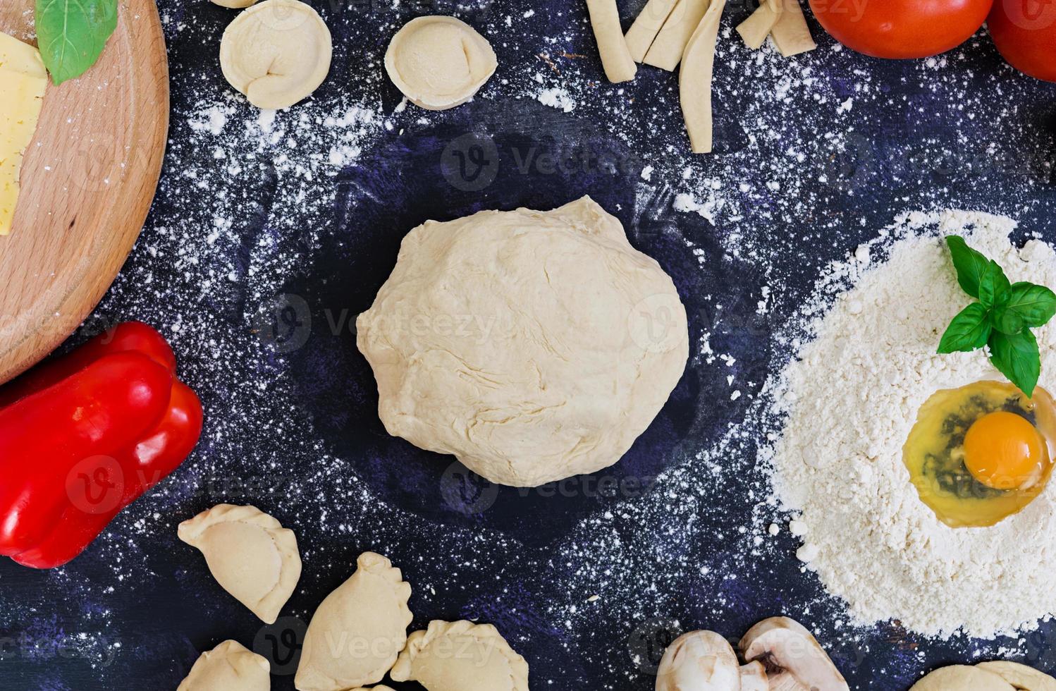 roher Pizzateig mit Zutaten und Gewürzen auf dunklem Hintergrund. Ansicht von oben foto