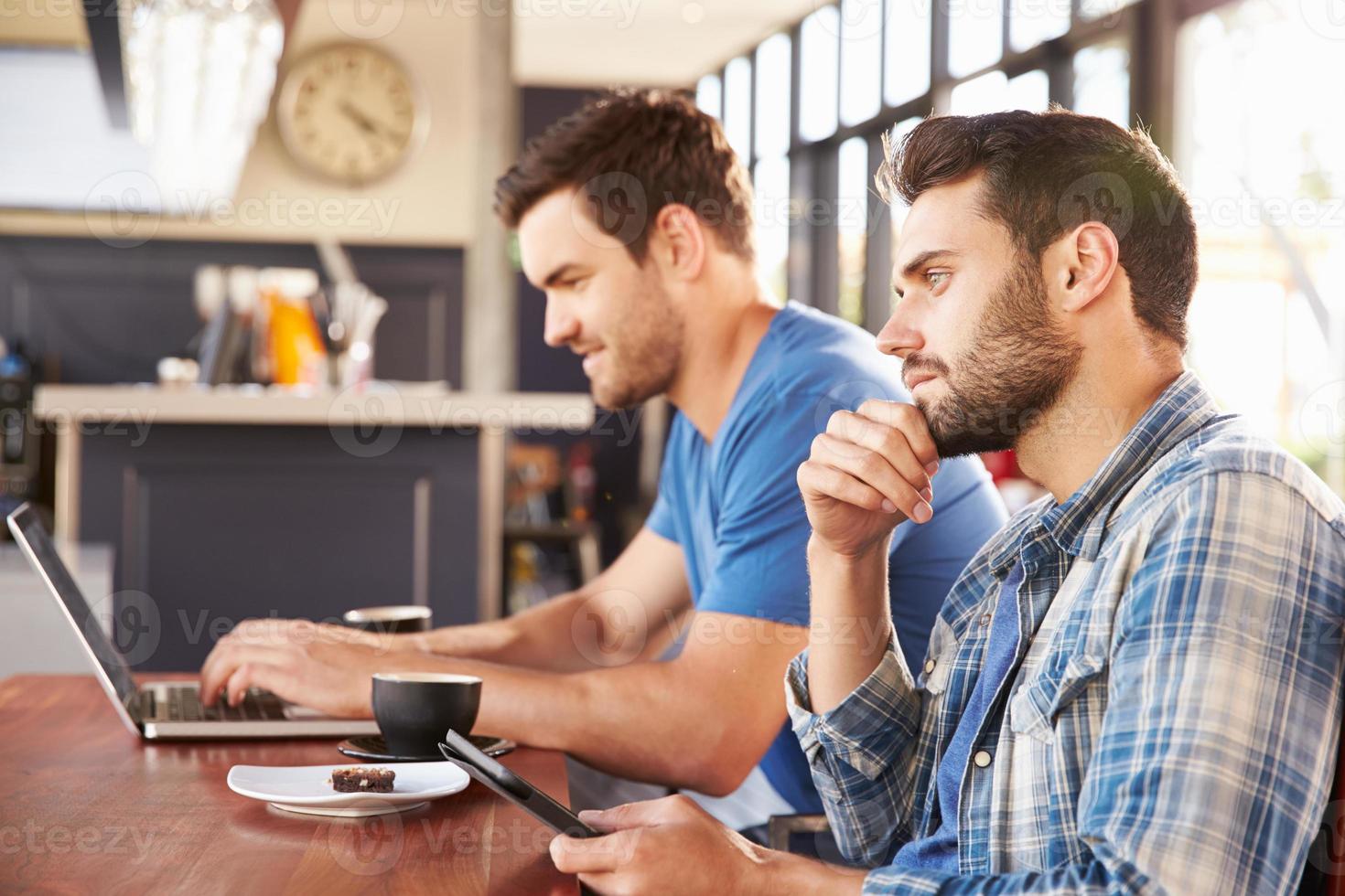 zwei junge Männer, die an Computern in einem Café arbeiten foto
