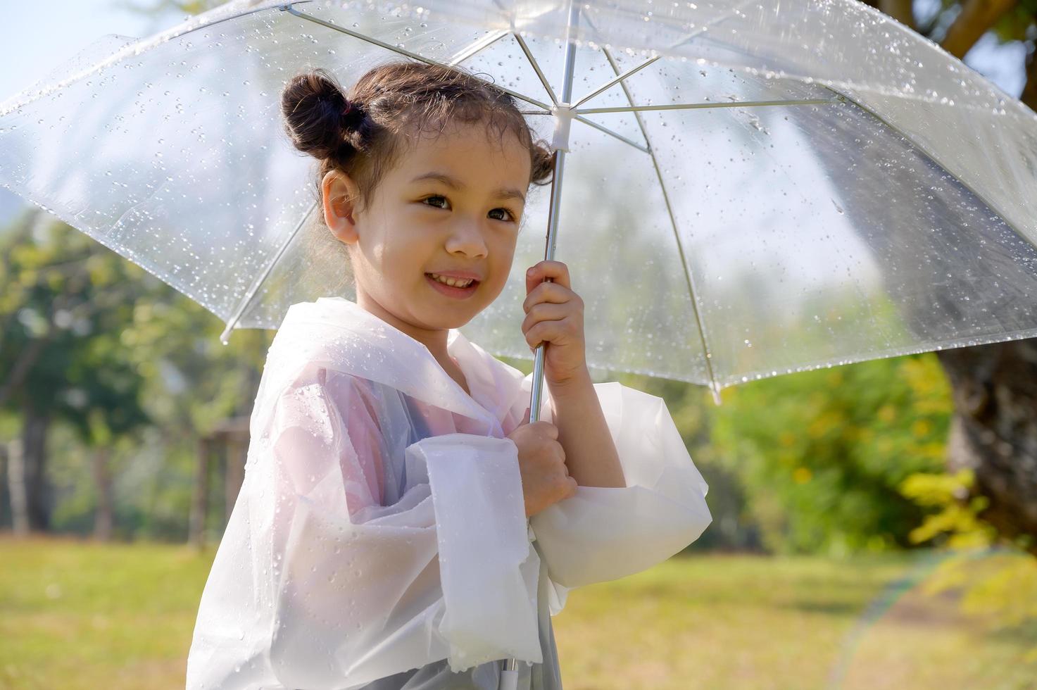 Ein kleines Mädchen stand glücklich in einem Regenschirm gegen den Regen foto