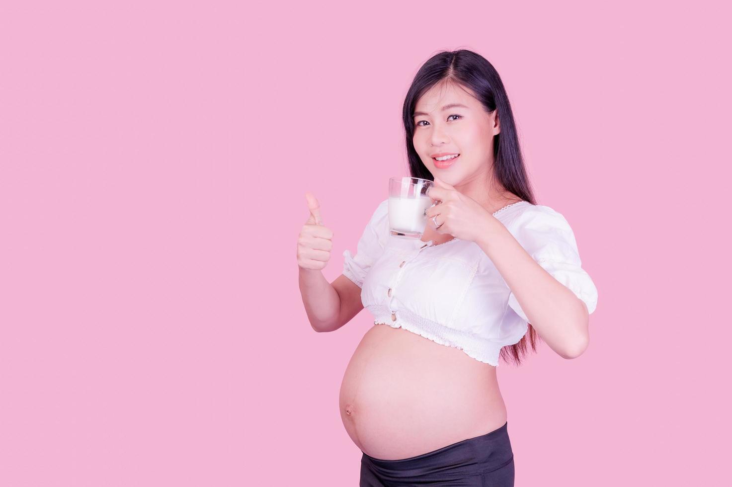 Eine schöne schwangere Frau steht und trinkt frische Milch für eine gute Gesundheit für ihr zukünftiges Baby foto