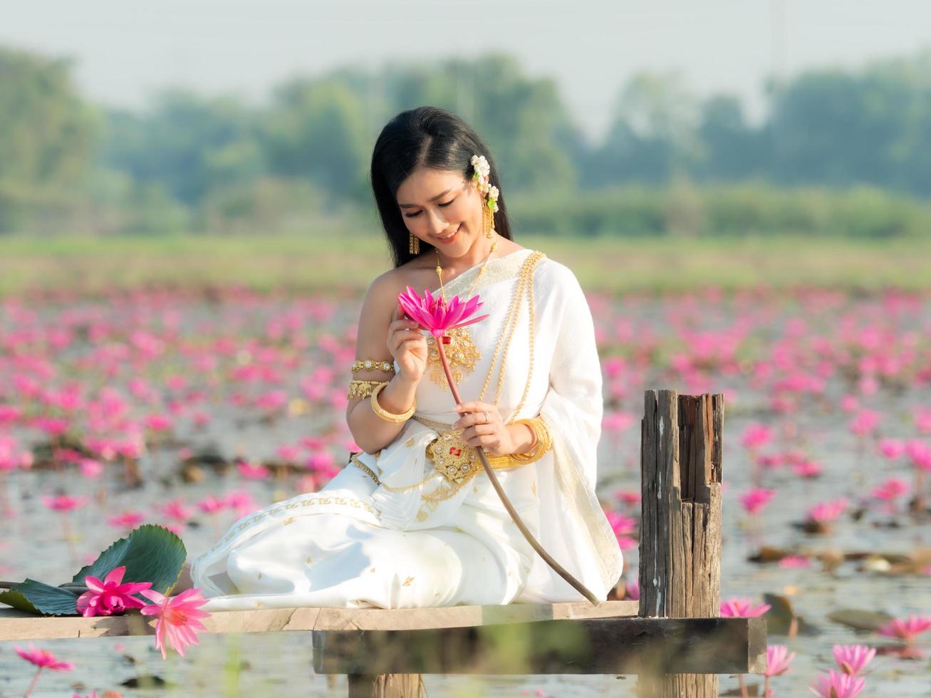 Eine elegante thailändische Frau, die traditionelle thailändische Kleidung trägt und Lotusblumen trägt, die von einem Lotusfeld gesammelt wurden foto