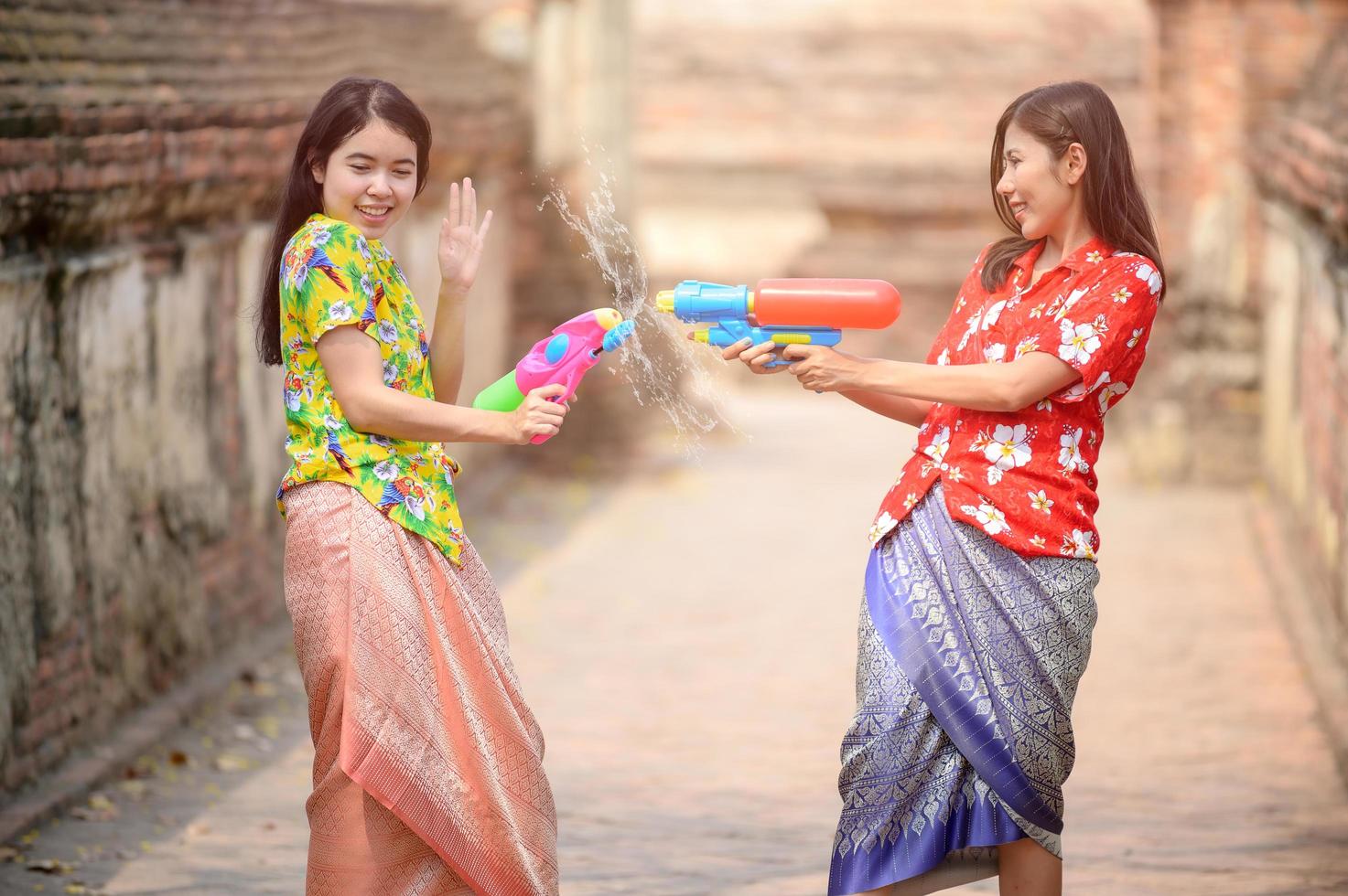 Schöne asiatische Frauen halten während Songkran, dem schönsten und lustigsten Wasserfest in Thailand, Plastikwasserpistolen in einem alten Tempel foto