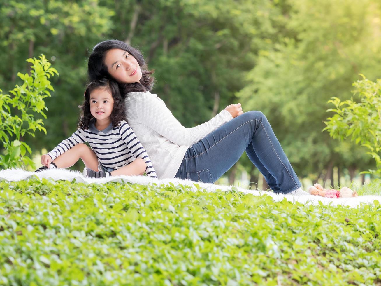 asiatische kleine Mädchen sitzen mit ihrer Mutter auf dem Teppich, entspannen und lernen außerhalb der Schule, um im Naturpark zu genießen foto