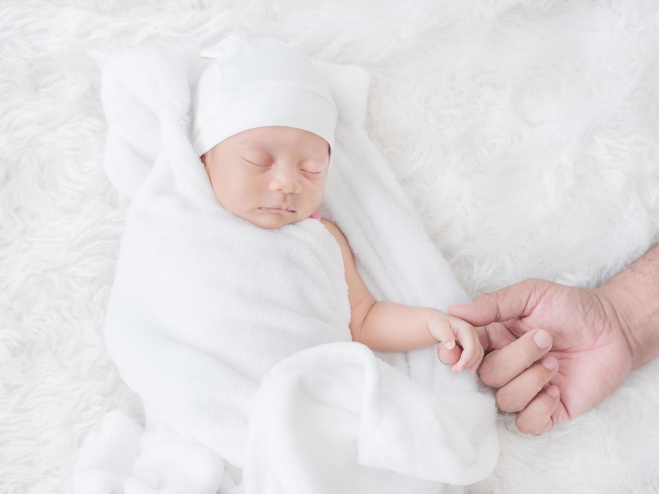 Neugeborenes Mädchen schläft warm auf dem weißen Tuch und berührt die Hand ihres Vaters mit Liebe foto