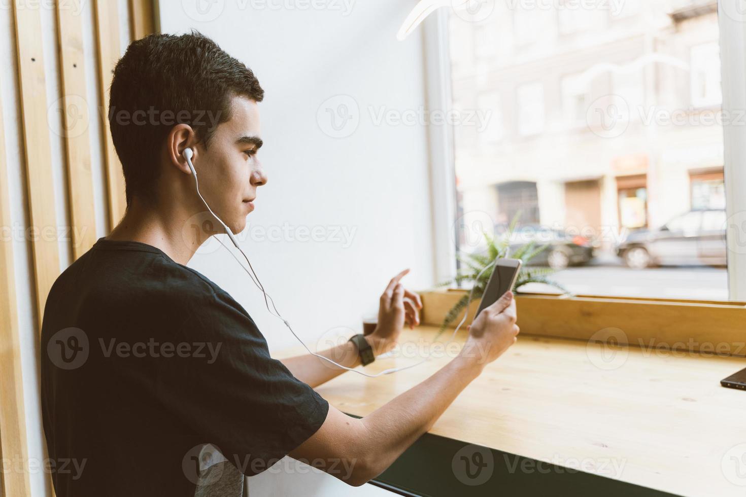 Textnachricht für junge Erwachsene auf dem Smartphone und Musik über Kopfhörer im Café hören. Lebensstil, Freizeit, Erholung, Entspannung foto