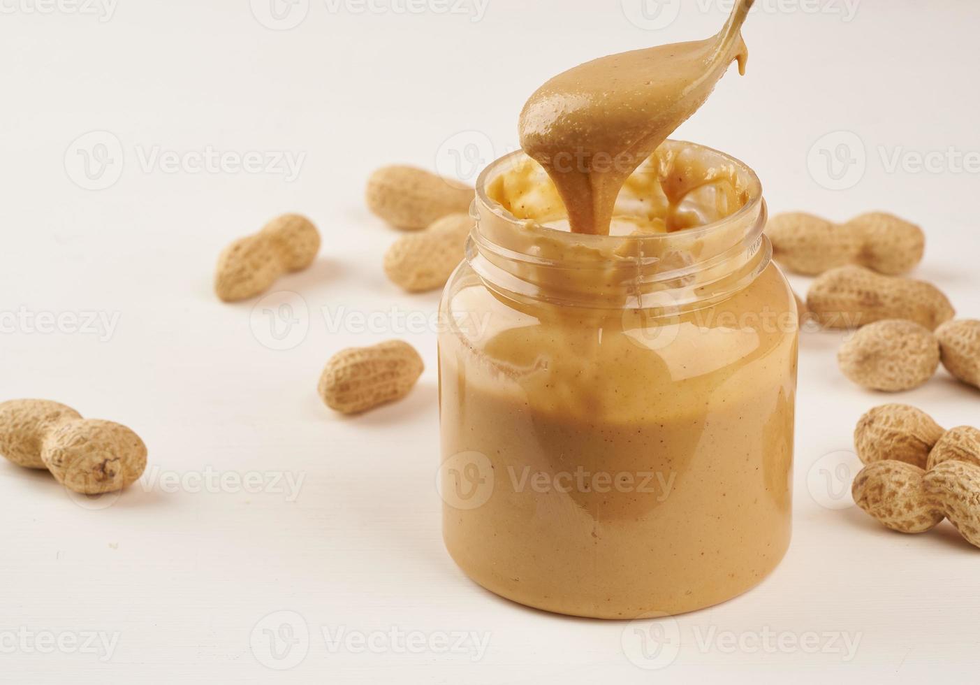 Glas Erdnussbutter und Erdnüsse in der Schale auf einem weißen Tisch, Seitenansicht, frisch gemahlene Nüsse, Seitenansicht foto