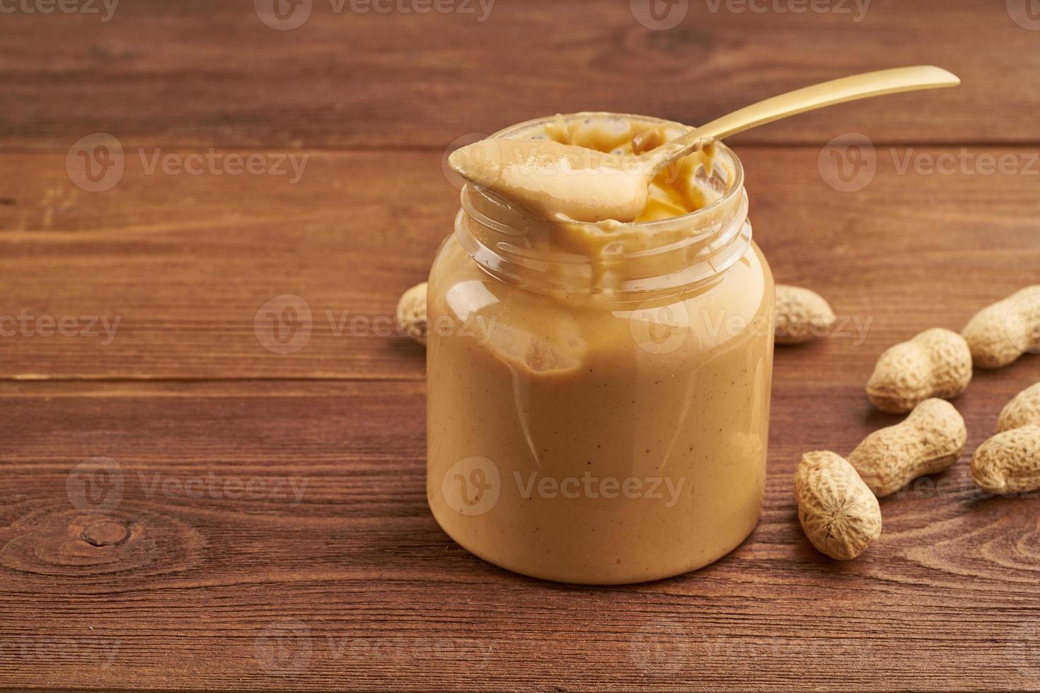 Glas Erdnussbutter und Erdnüsse in einer Schale auf braunem Holztisch foto