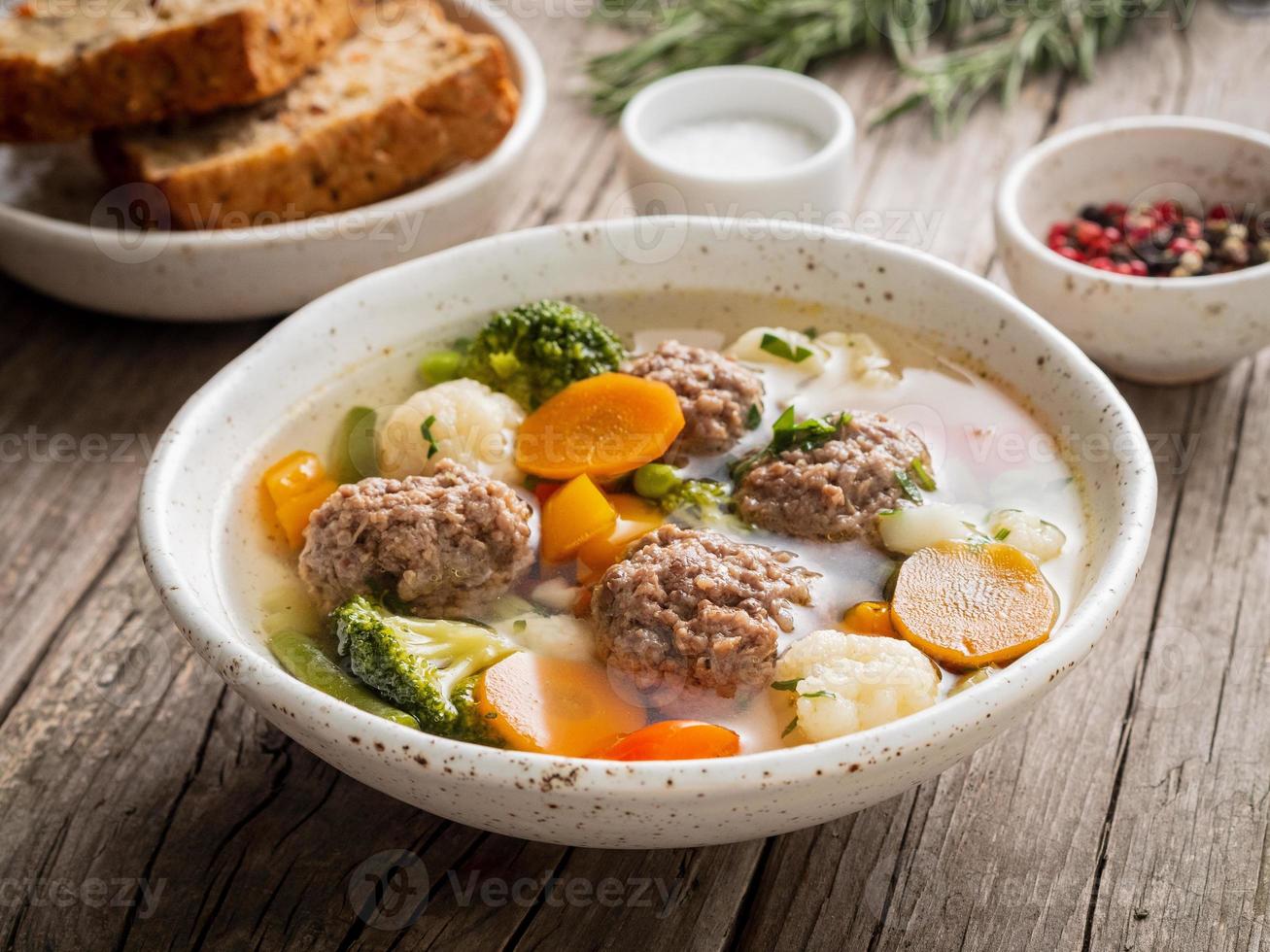 Frikadellensuppe in weißer Platte auf altem rustikalem grauem Holztisch, Seitenansicht foto