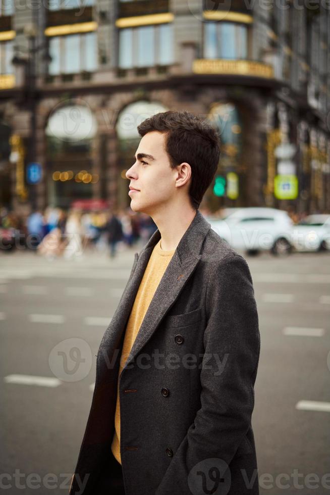 gutaussehender, stilvoller, modischer mann, brünett im eleganten grauen mantel, steht auf der straße im historischen zentrum von st. petersburg. junger Mann mit dunklen Haaren, dicken Augenbrauen. foto