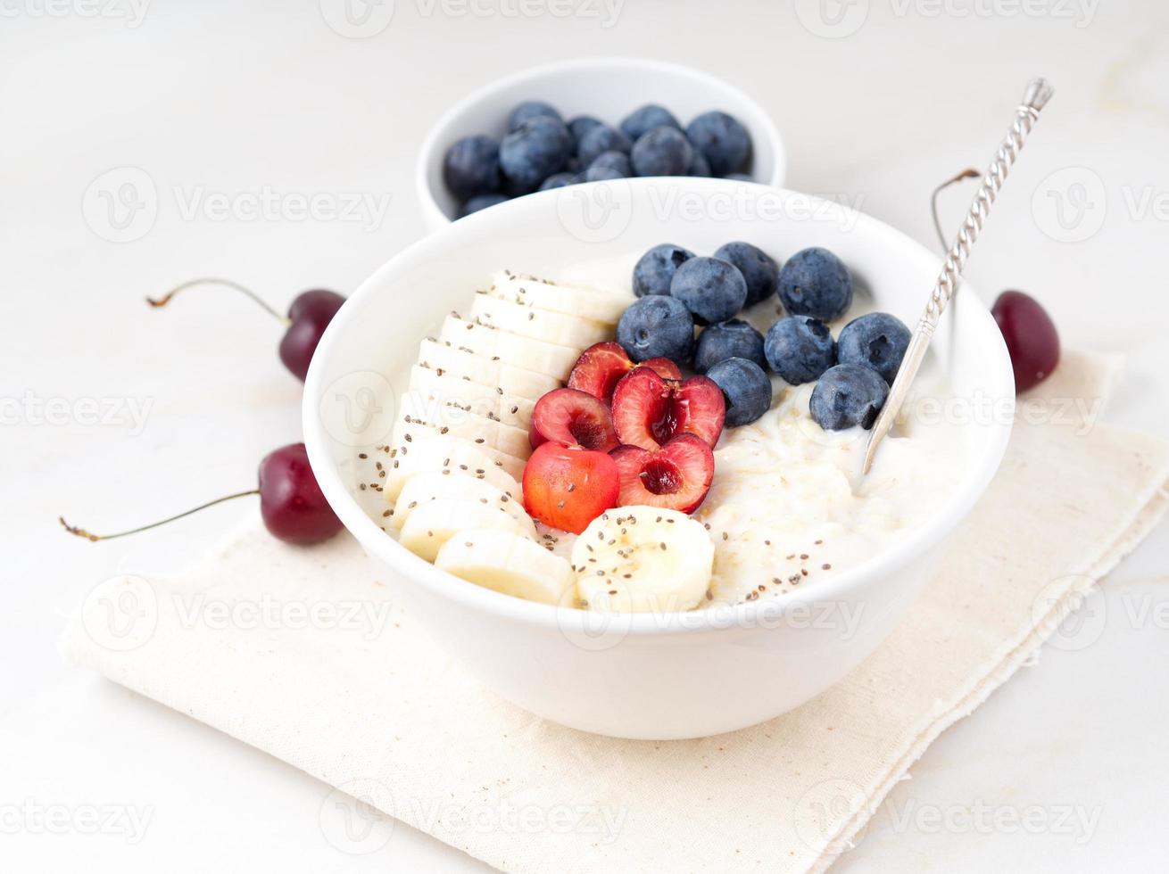 Große Schüssel mit leckeren und gesunden Haferflocken mit Früchten und Beeren zum Frühstück, Morgenmahlzeit. Seitenansicht, weißer Marmortisch foto