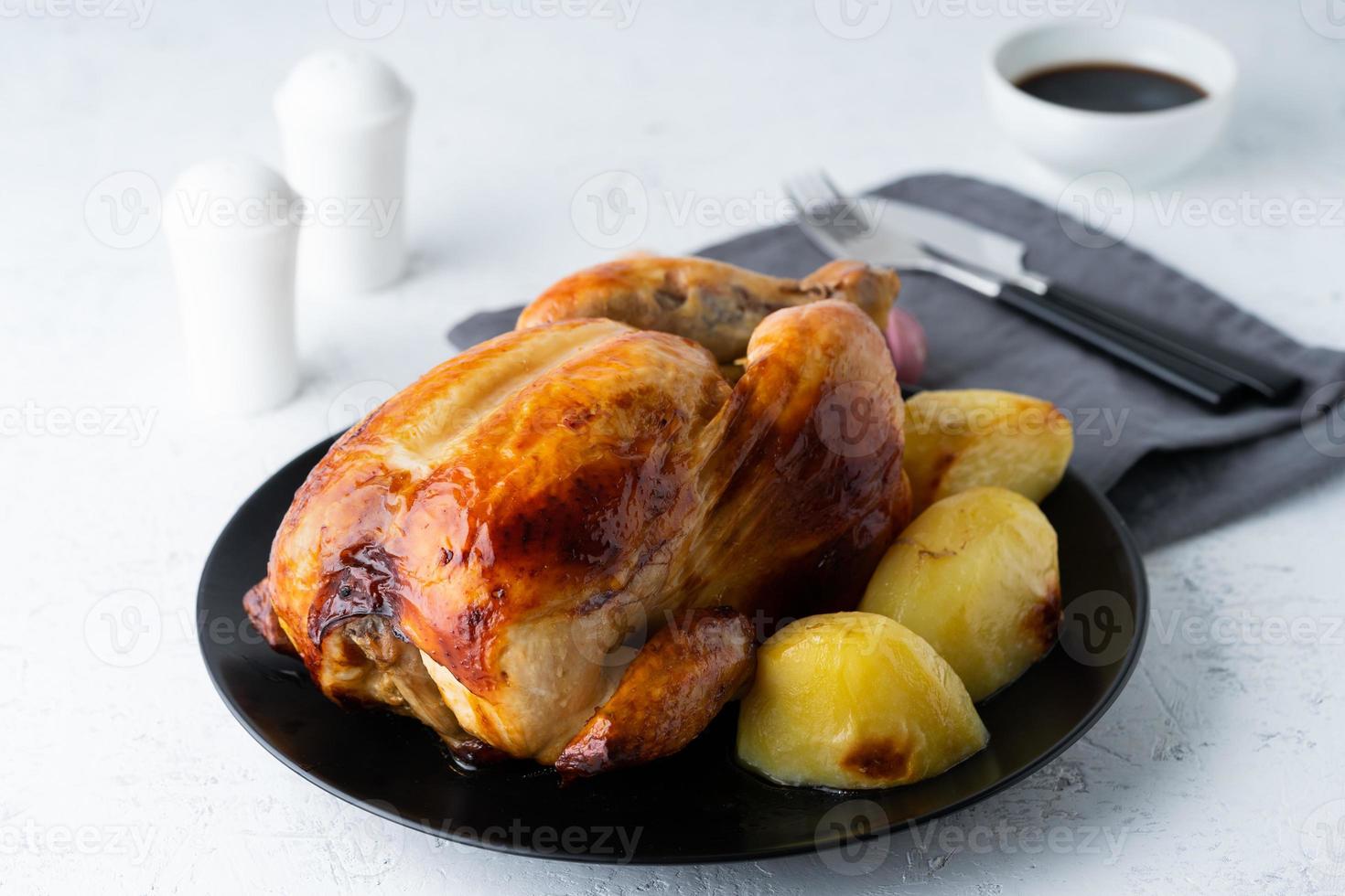 gegrilltes ganzes huhn in schwarzer platte auf weißem tisch, gebackenes fleisch mit kartoffeln. Seitenansicht foto