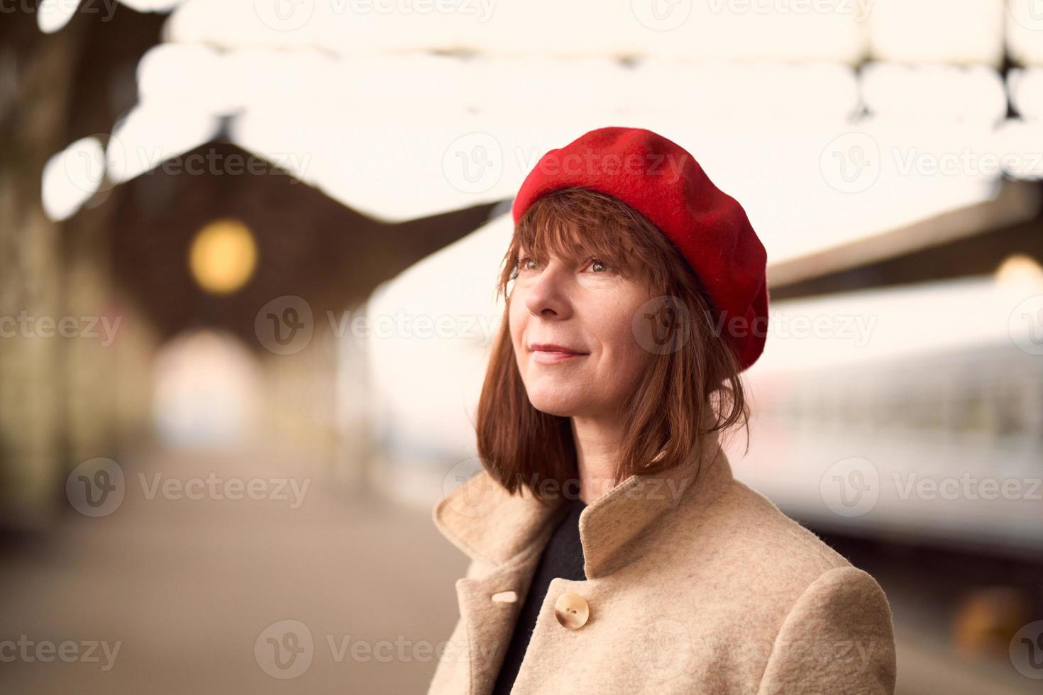 Nahaufnahme Porträt einer schönen Frau, die lächelt und auf den Zug am Bahnhof wartet. Mädchen reist mit leichtem Gepäck foto