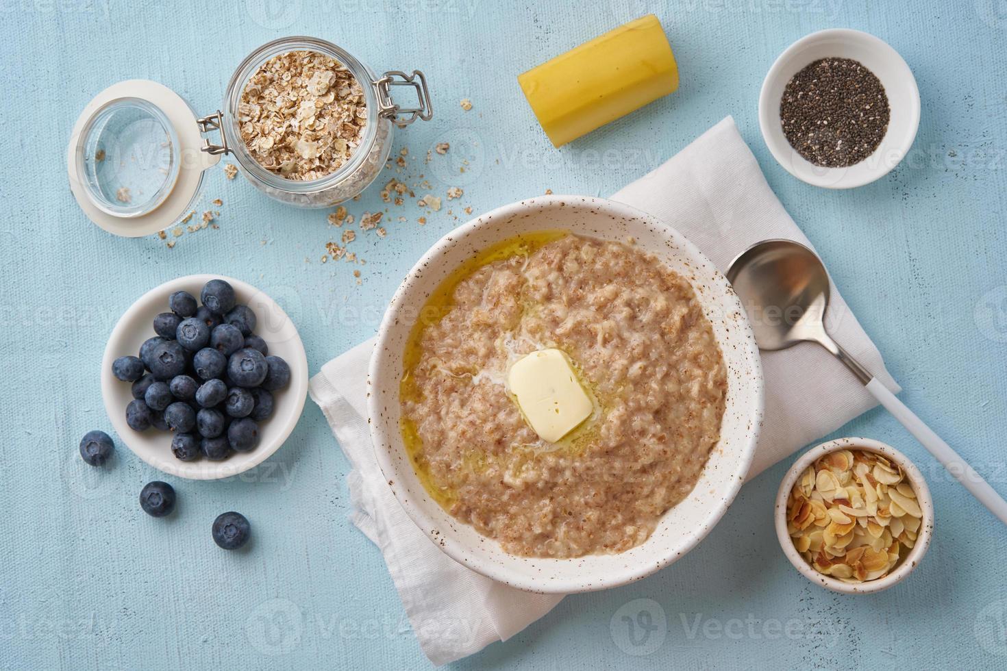 Haferflocken mit Butter und Toppings. Heidelbeeren, Chiasamen, Mandelflocken, Banane. Ansicht von oben foto