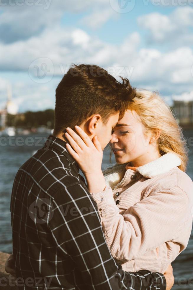 Der Junge sieht das Mädchen zärtlich an und will es küssen. Ein junges Paar umarmt sich. das Konzept der Jugendliebe und des ersten Kusses, aufrichtige Gefühle von Mann und Frau. die Stadt, die Uferpromenade. foto