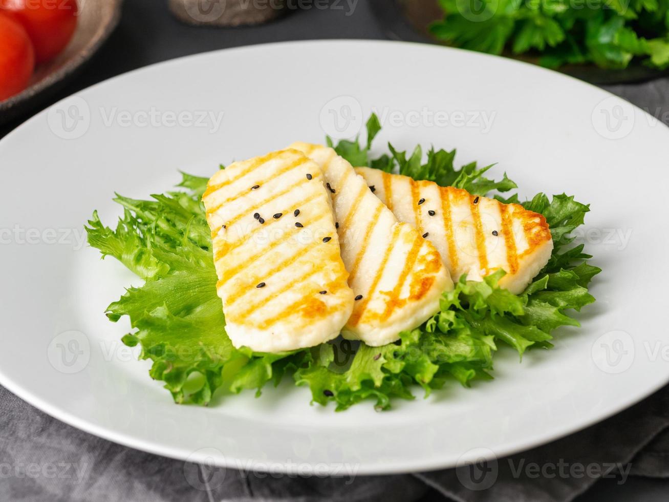 gegrillter Halloumi, gebratener Käse mit Kopfsalat. ausgewogene Ernährung, weiße Platte auf dunklem Hintergrund, Seitenansicht foto