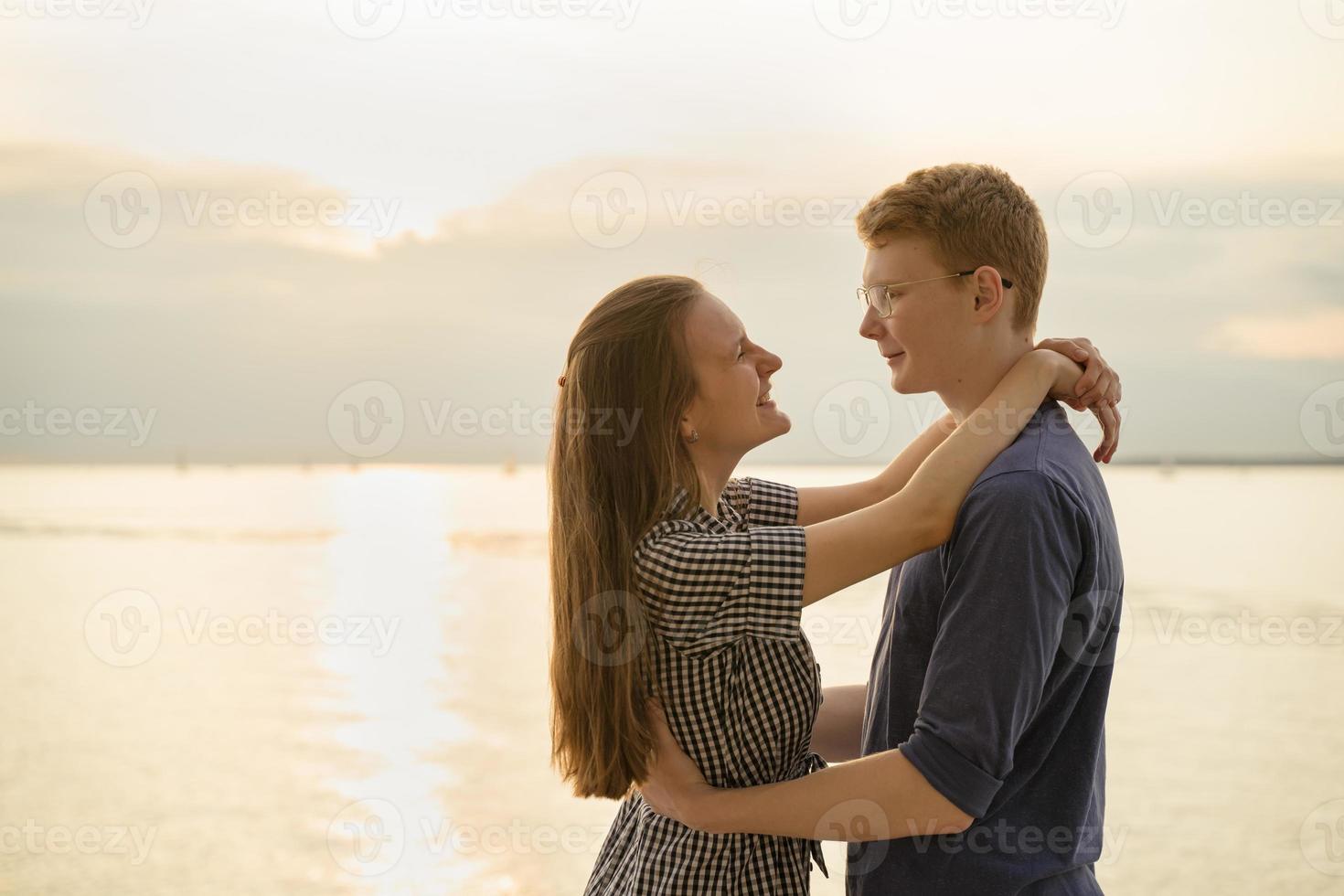 Teenager sehen sich am Strand, bewölktem Wetter und Sonnenuntergang im Hintergrund an foto