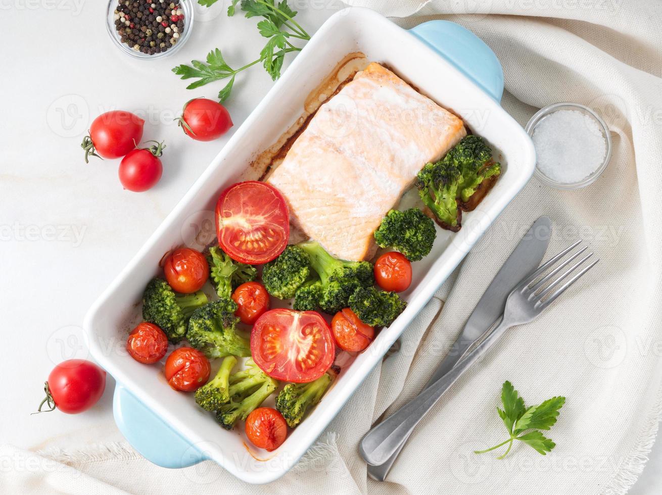 im ofen gebackener fischlachs mit gemüse - brokkoli, tomaten. gesunde diätnahrung, weißer marmorhintergrund, draufsicht. foto