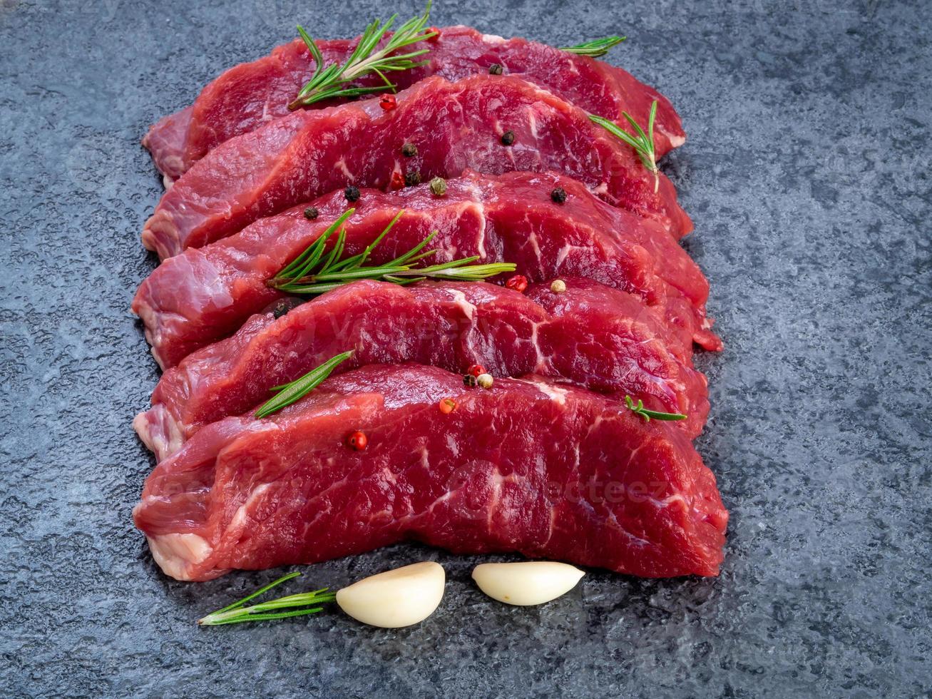 rohes Fleisch, Rindersteak mit Gewürzen auf einem schwarzen Steintisch, Seitenansicht foto