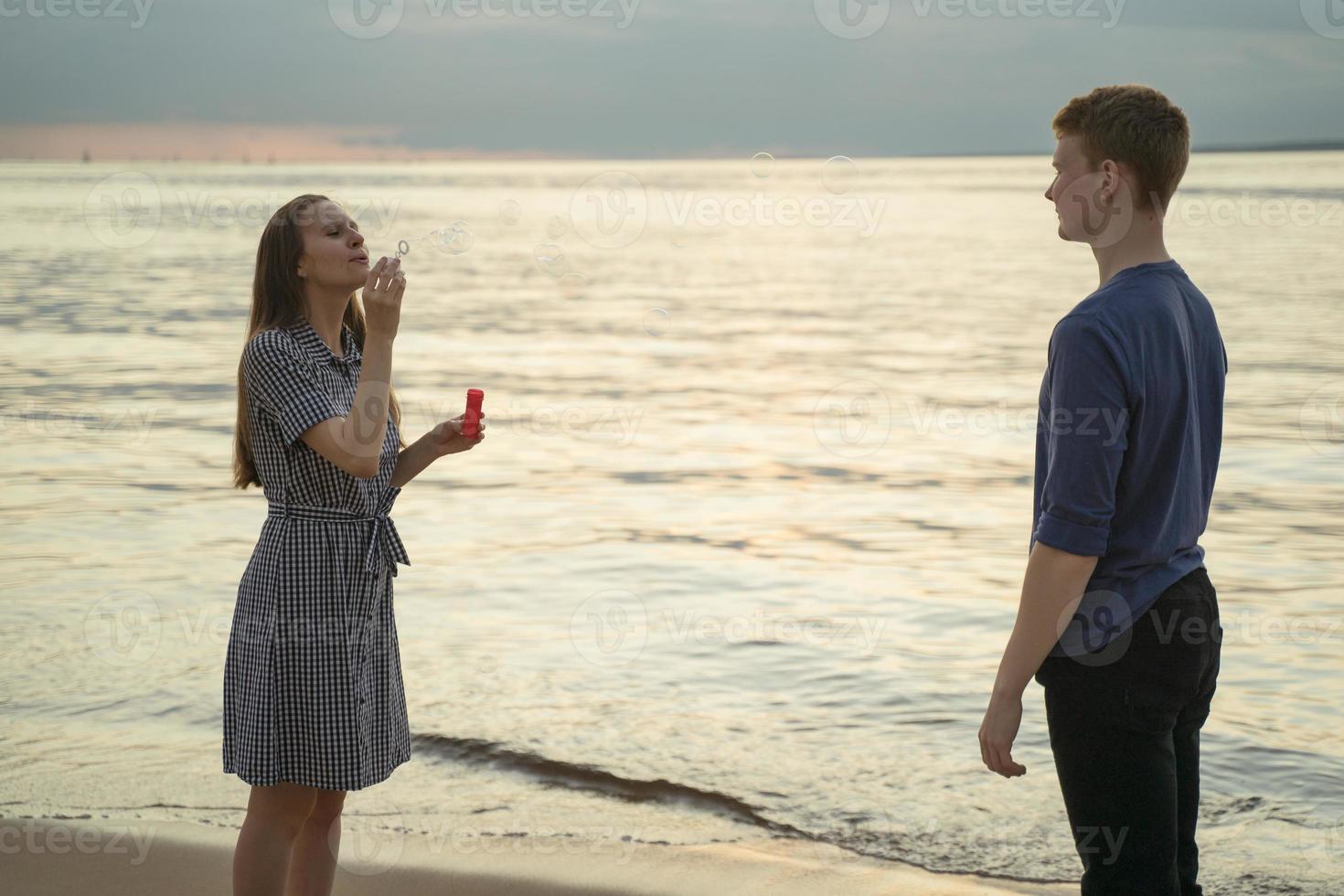 Mädchen bläst Seifenblasen und Junge schaut sie an, Strand im Hintergrund foto