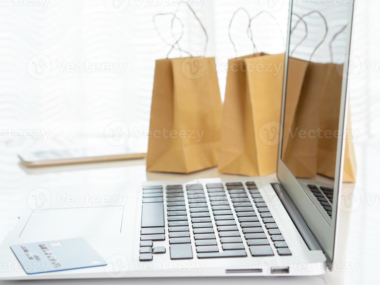 Bastelpakete mit Einkäufen, Laptop-Smartphone, Kreditkarte auf dem Tisch vor dem Fenster, Online-Shopping-Konzept foto
