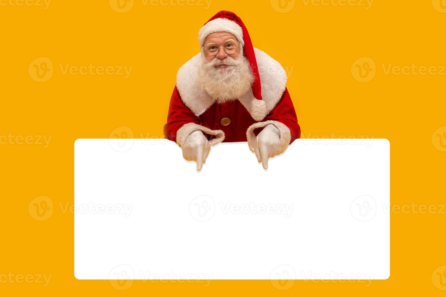 glücklicher weihnachtsmann, der hinter dem leeren schild herausschaut, das auf gelbem hintergrund mit kopienraum isoliert ist foto