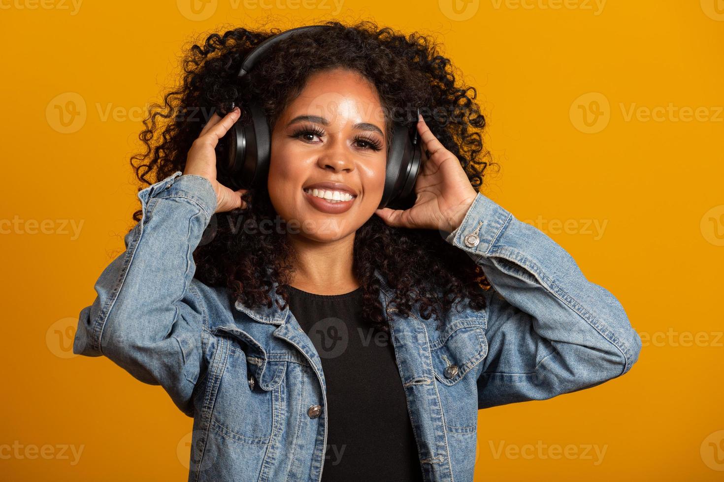 menschen, musik, emotionen konzept. Entzückte sorglose Frau mit Afro-Frisur tanzt im Rhythmus der Melodie, schließt die Augen und hört lautes Lied im Kopfhörer. schöne afro-frau mit ihren kopfhörern foto