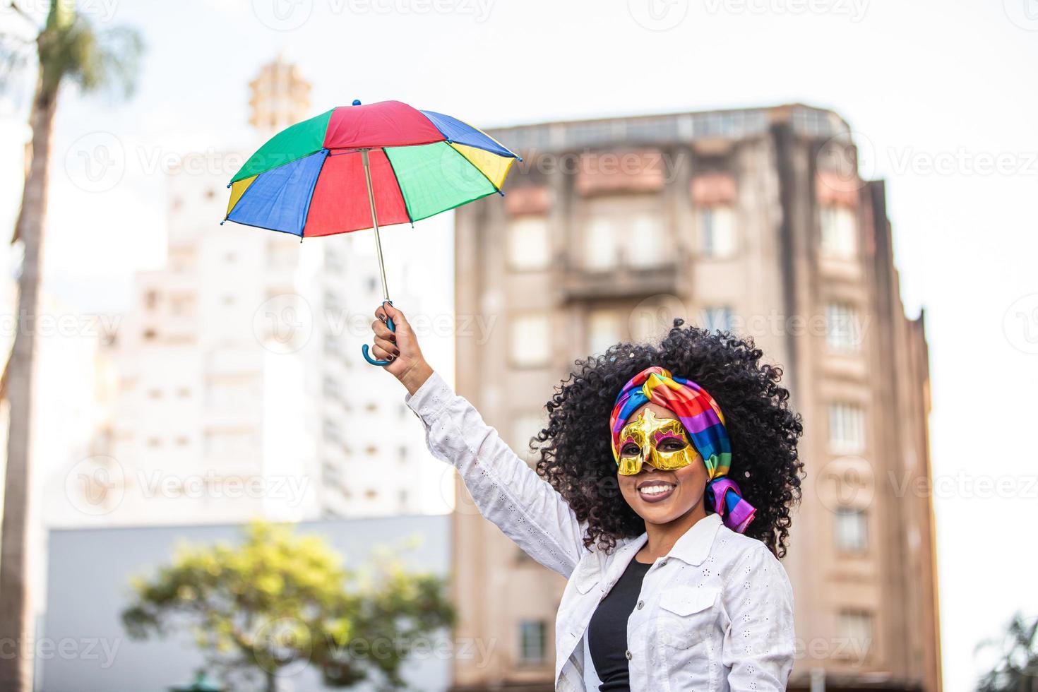 junge lockige haarfrau, die die brasilianische karnevalsparty mit frevo-regenschirm auf der straße feiert. foto