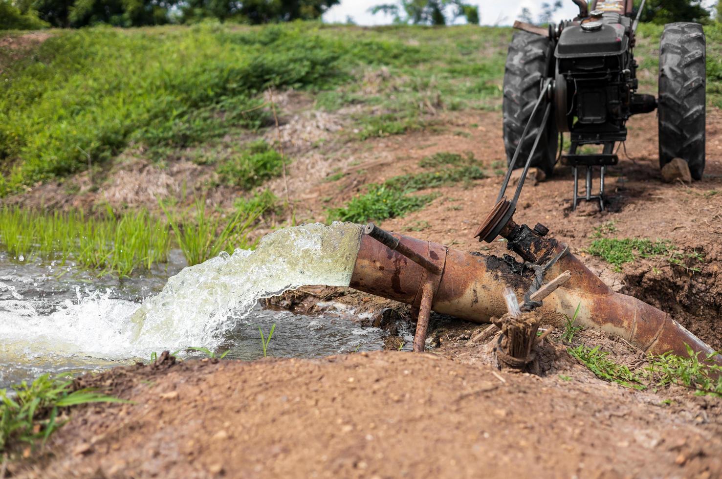 Wasser strömt aus Stahlrohren in grüne Reisfelder und landwirtschaftliche Fahrzeuge. foto