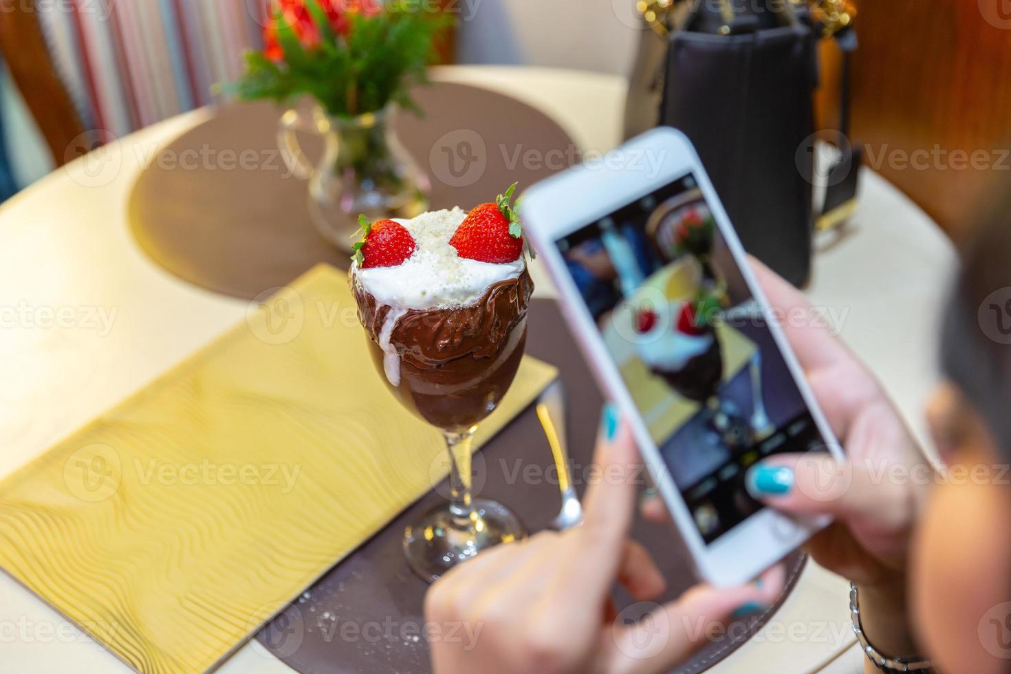 Frau fotografiert köstliches Eis mit weißen Mischungen Erdbeere mit einem Smartphone. foto