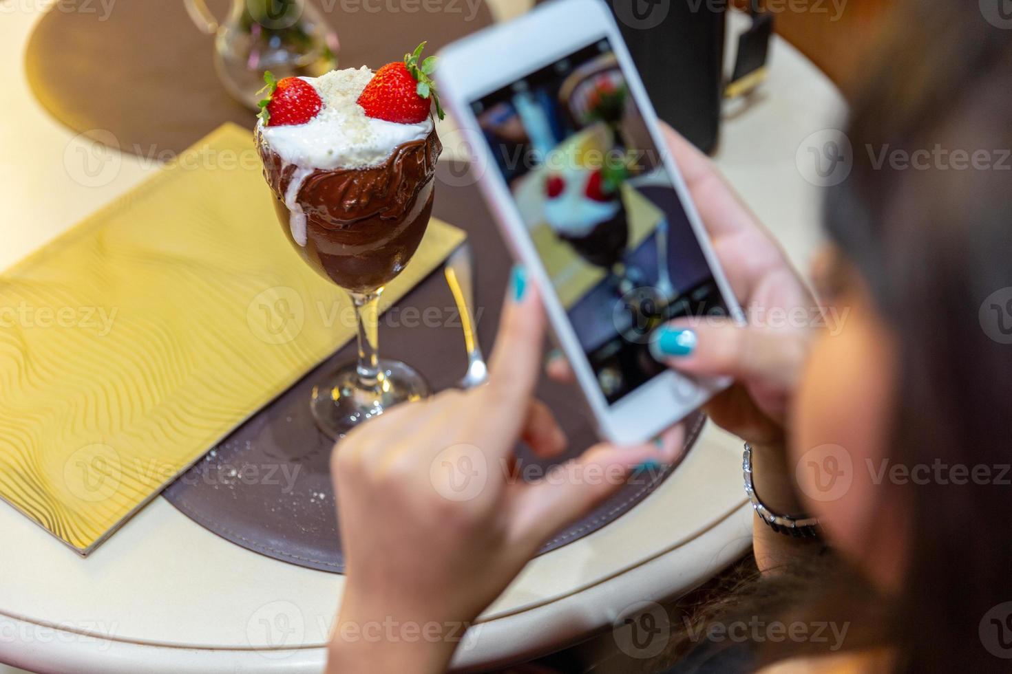 Frau fotografiert köstliches Eis mit weißen Mischungen Erdbeere mit einem Smartphone. foto