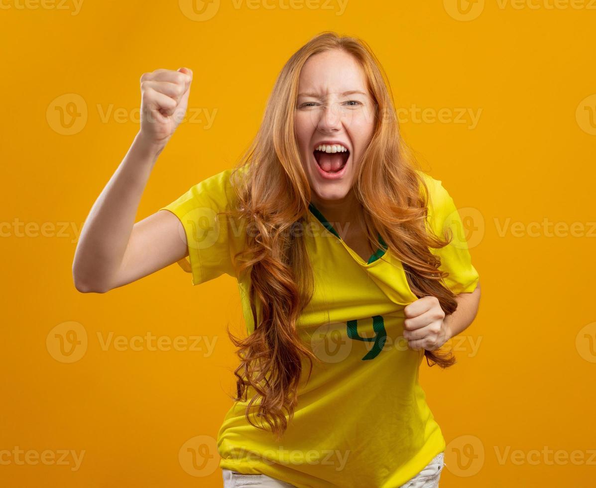 Brasilien Unterstützer. brasilianischer rothaariger frauenfan, der auf fußball, fußballspiel auf gelbem hintergrund feiert. Brasilien Farben. foto