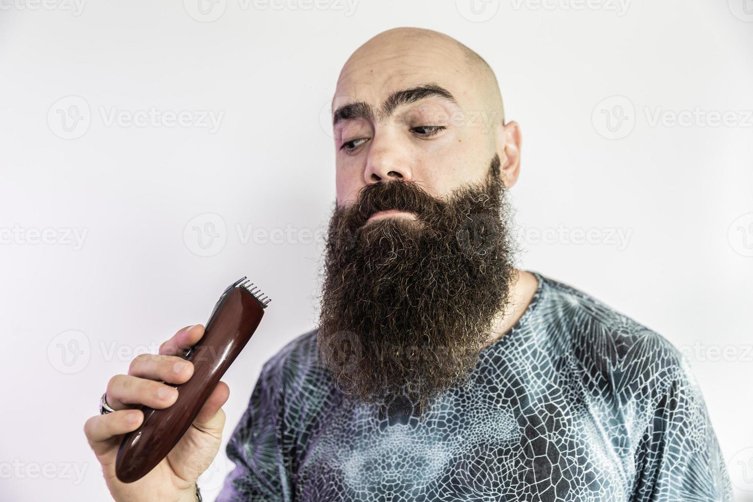 Ein bärtiger Mann wird seinen Bart mit einem elektronischen Rasierer rasieren foto