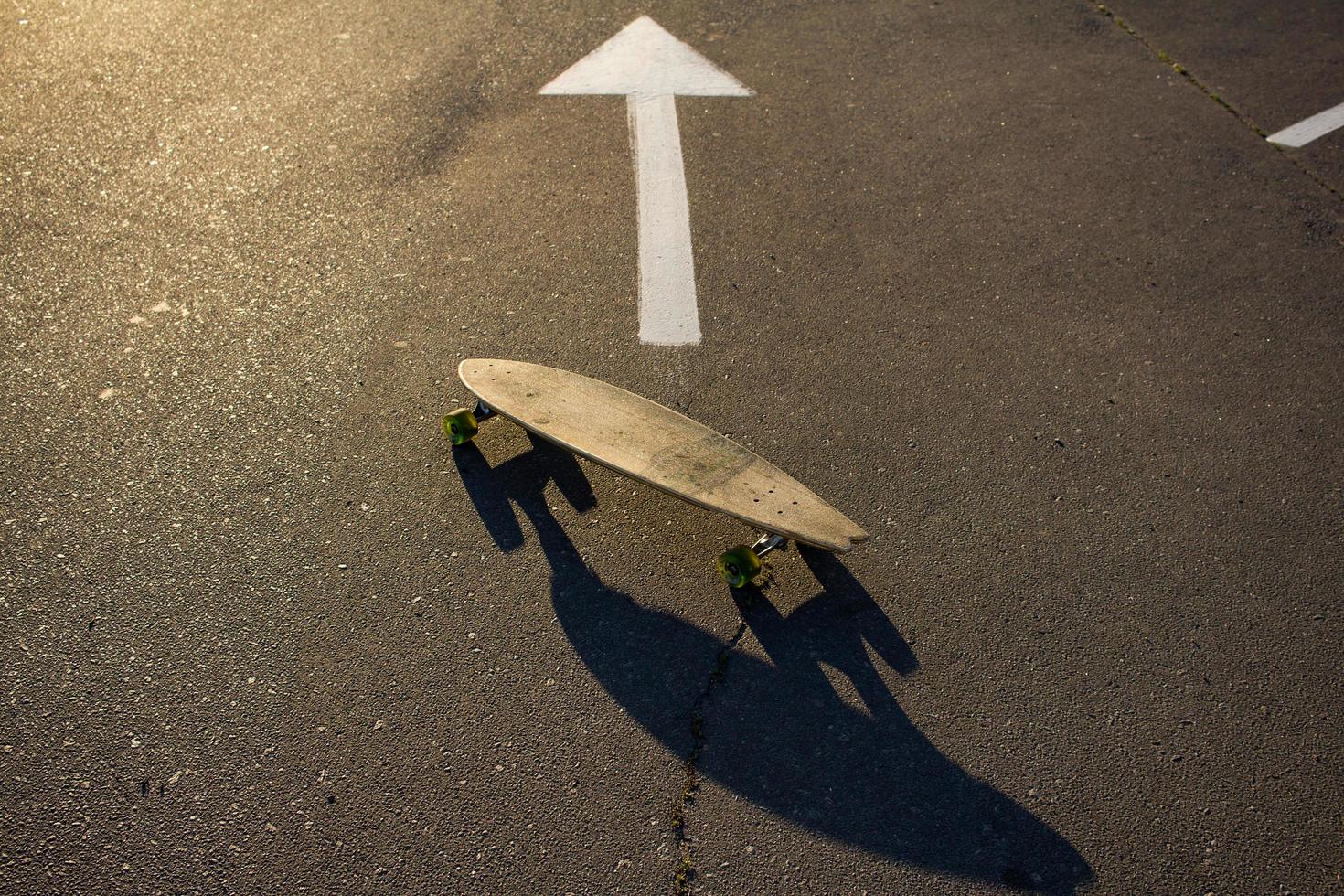 Longboard-Skate steht allein auf Asphalt im gelben Sonnenlicht foto