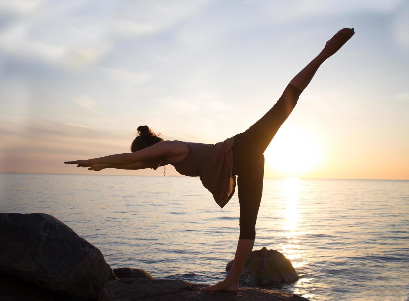 asiatische frau der fitness gemischten rasse in yoga-pose am morgenstrand, schöne fitte frau übt fitness exrxise steine, morgenmeer oder ozean hintergrund foto