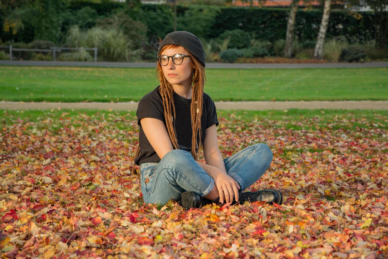 junge Frau mit roten Dreadlocks und Brille, die sich im Herbstpark entspannt foto