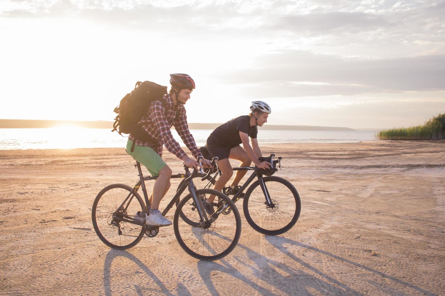 Zwei junge Männer auf einem Tourenrad mit Rucksäcken und Helmen in der Wüste auf einer Fahrradtour foto