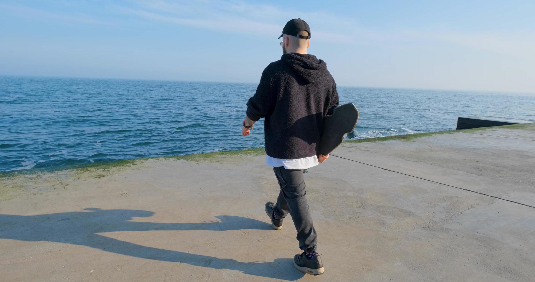 junger Mann mit Skateboard, der sich in der Nähe des Meeres entspannt foto