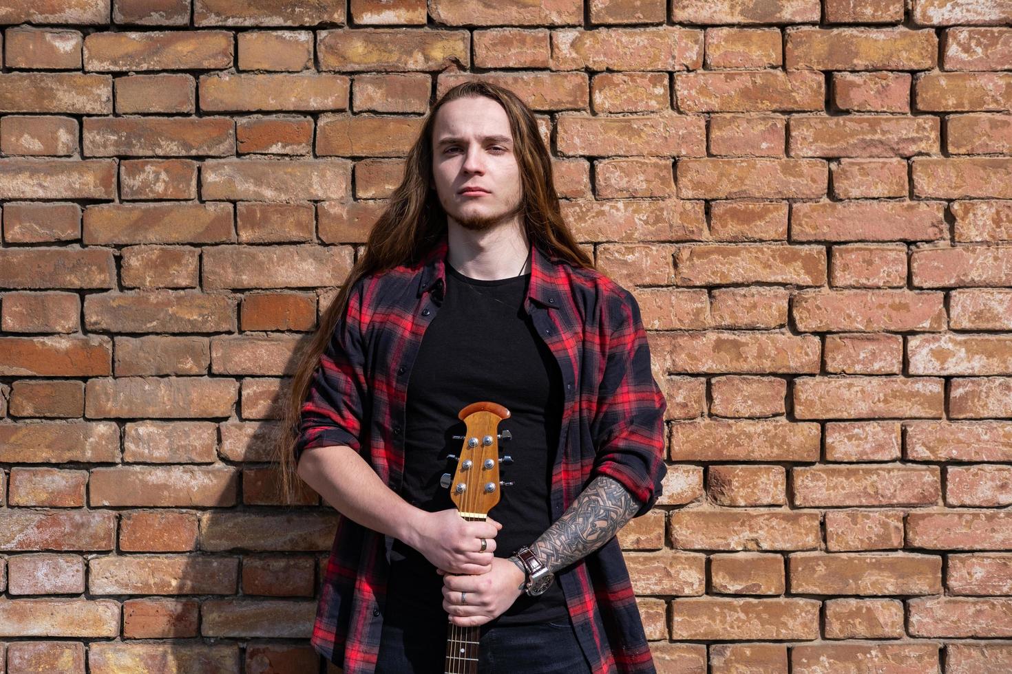 junger mann mit langen haaren und tätowierung spielt auf der akustikgitarre im freien auf der straße foto