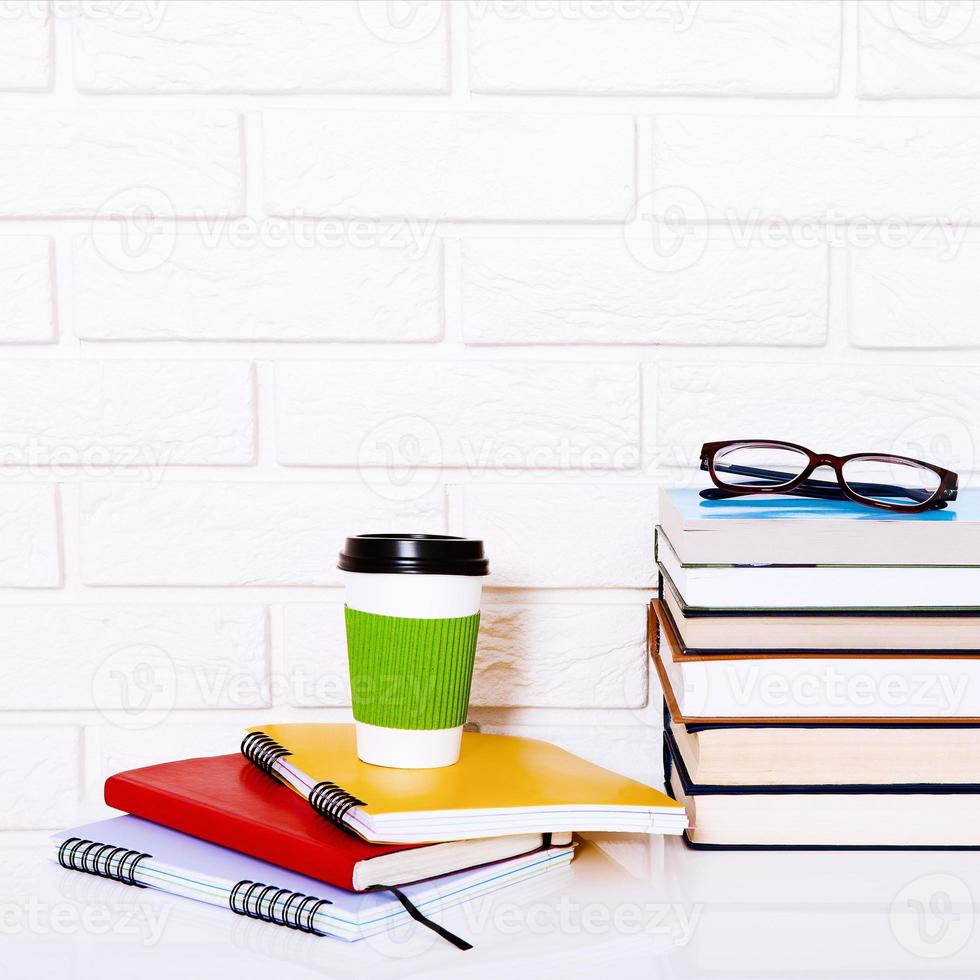 arbeitsplatz- und bildungszubehör auf dem tisch. Tasse Kaffee, Bücher, Gläser, Notizbücher. Stammausbildung und schulischer Hintergrund. foto