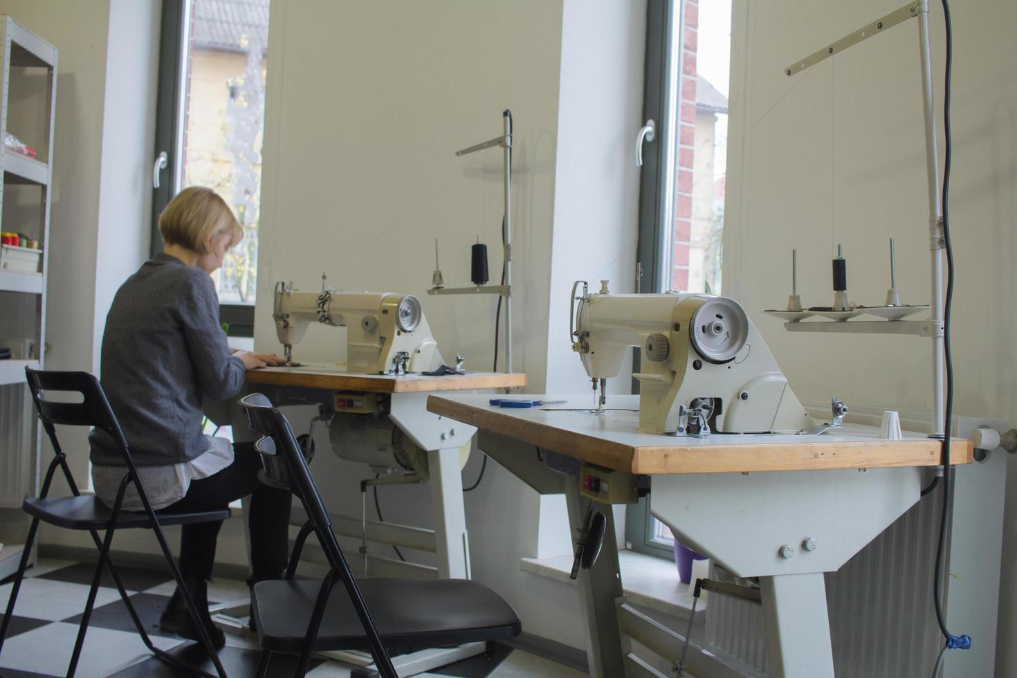 Näherin bei der Arbeit auf dem Tisch, Schneiderfrau arbeitet im Studio mit Kleidung foto