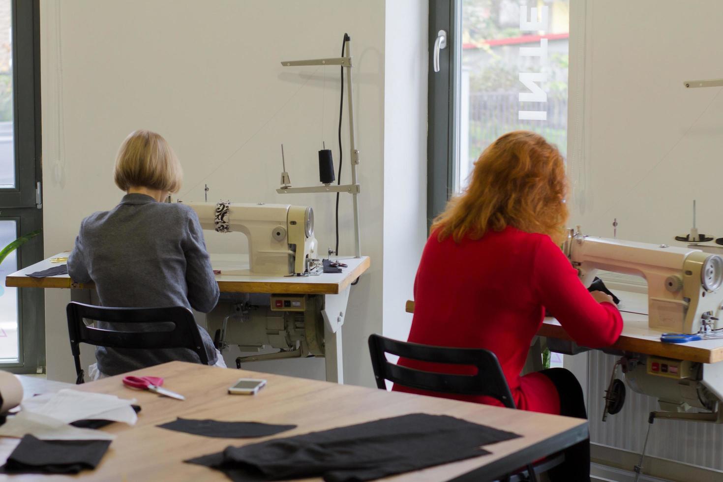 Näherin bei der Arbeit auf dem Tisch, Schneiderfrau arbeitet im Studio mit Kleidung foto