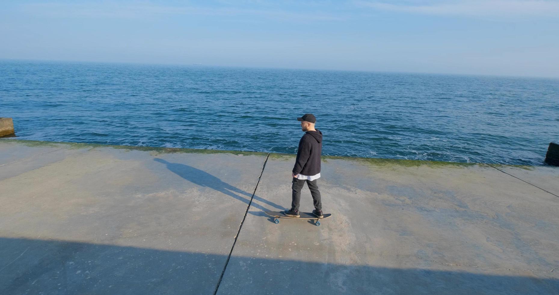 junger Mann mit Skateboard, der sich in der Nähe des Meeres entspannt foto