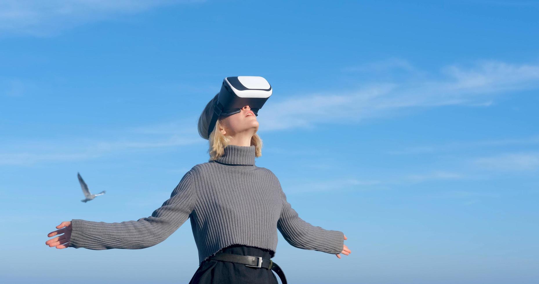 junge hübsche Frau mit Virtual-Reality-Brille im Freien am Strand gegen sonnigen blauen Himmel foto