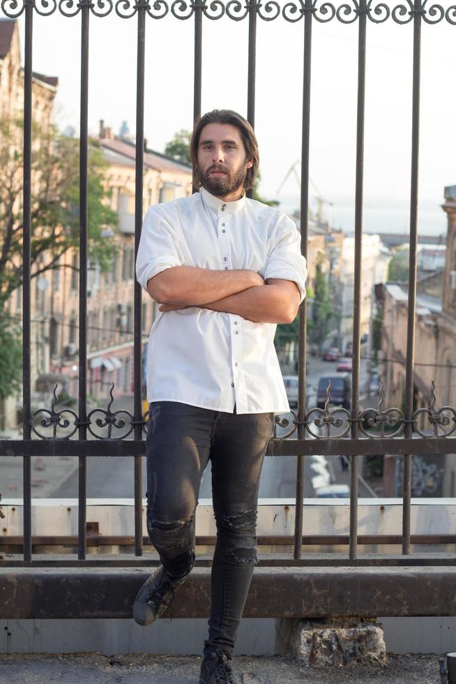 Porträt eines bärtigen Mannes in weißem Hemd, urbaner Hintergrund, Hipster, der auf der Brücke posiert foto