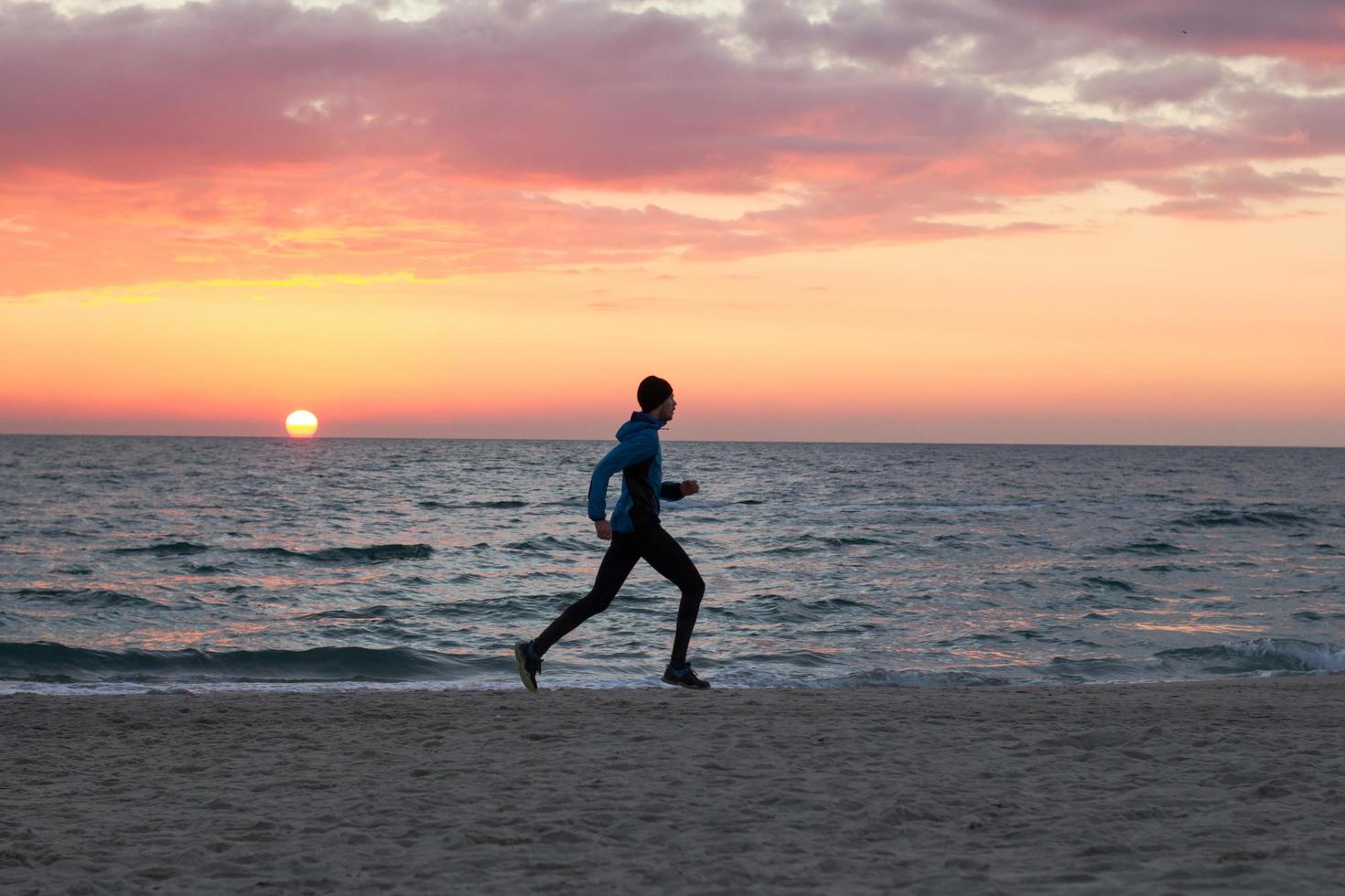 junger mann in herbstkleidung training am strand, sonnenaufgang hintergrund, männlicher läufer am morgen foto